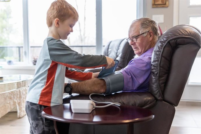 Archivo - Niño revisando la presión arterial de su abuelo en casa