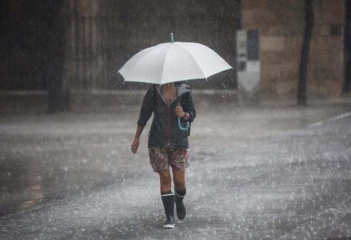 Archivo - Arxiu - Una persona camina amb un paraigua baix la pluja en imatge d'arxiu