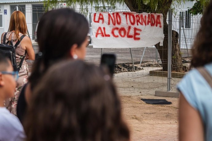 Diverses persones amb pancartes, durant una roda de premsa en una protesta pel no inici del curs, enfront dels barracons de Ceip Lluis Vives i l'Escola Infantil Ausiàs March de Massanassa, a 8 d'agost de 2025. 