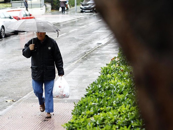 Archivo - Un hombre carga con su boplsa de la compra resguardado bajo su paraguas debido a las lluvias.