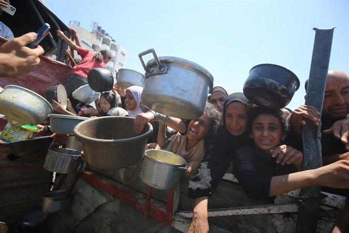 Archivo - Palestinos esperan a recibir alimentos de una organización caritativa en medio de la ofensiva de Israel contra la Franja de Gaza y de sus restricciones a la entrega de ayuda humanitaria (archivo)