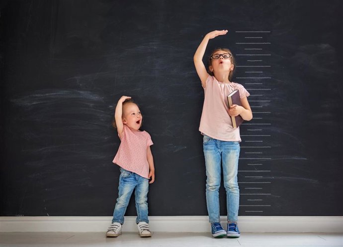 Archivo - Two children sisters play together. Kid measures the growth on the background of blackboard. Concept of education.