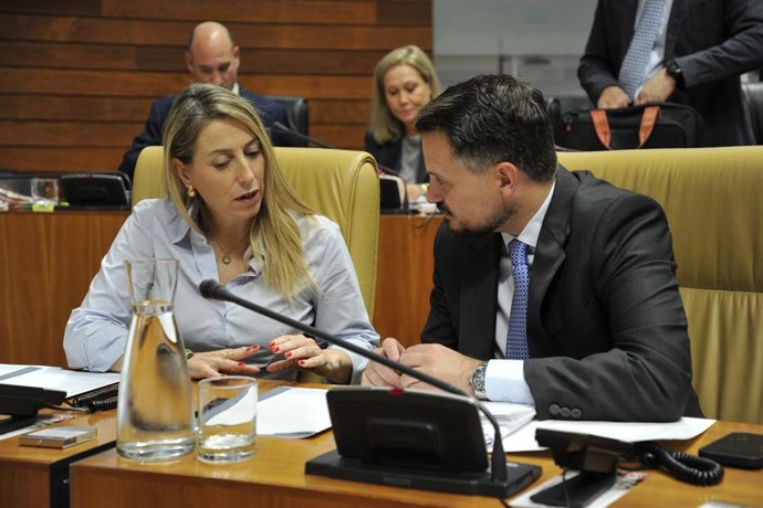 La presidenta de la Junta, María Guardiola, y el consejero de Presidencia, Abel Bautista, dialogan en sus escaños en el pleno de la Asamblea de Extremadura.