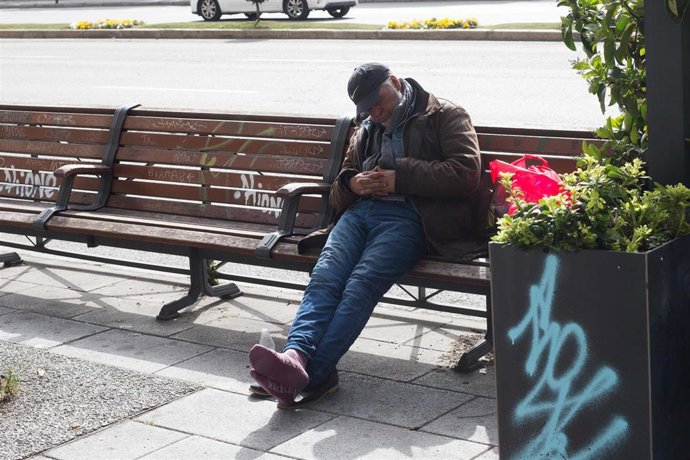 Archivo - Una persona sin hogar duerme sentada en un banco, en Madrid (España).