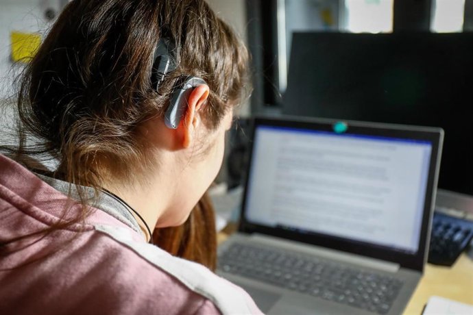 Archivo - Una joven usuaria de audífonos estudiando con un ordenador.