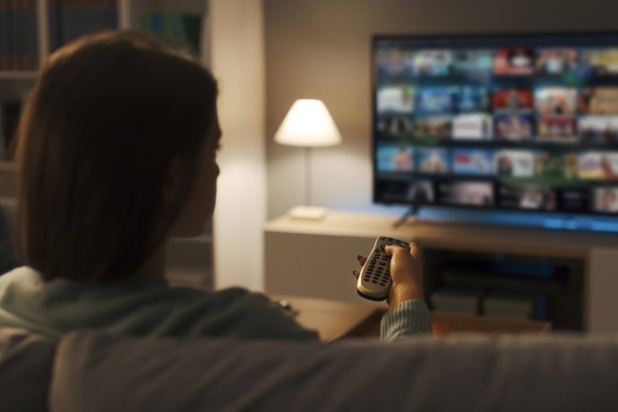 Archivo - Mujer joven eligiendo una serie en el televisor.