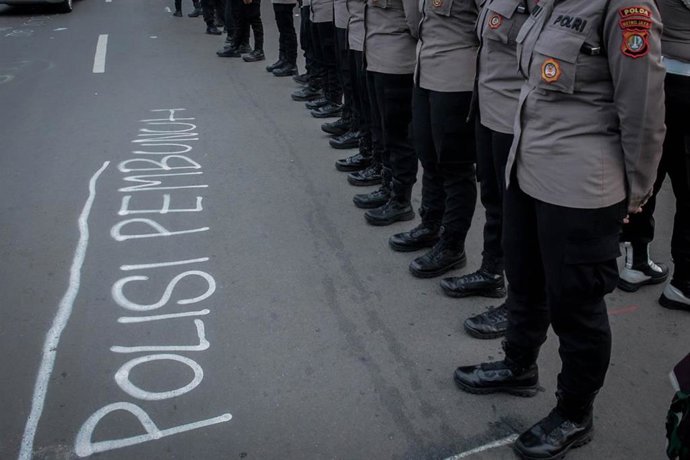 Agentes de la Policía en Indonesia frente a una pintada con la frase "Policía asesina"
