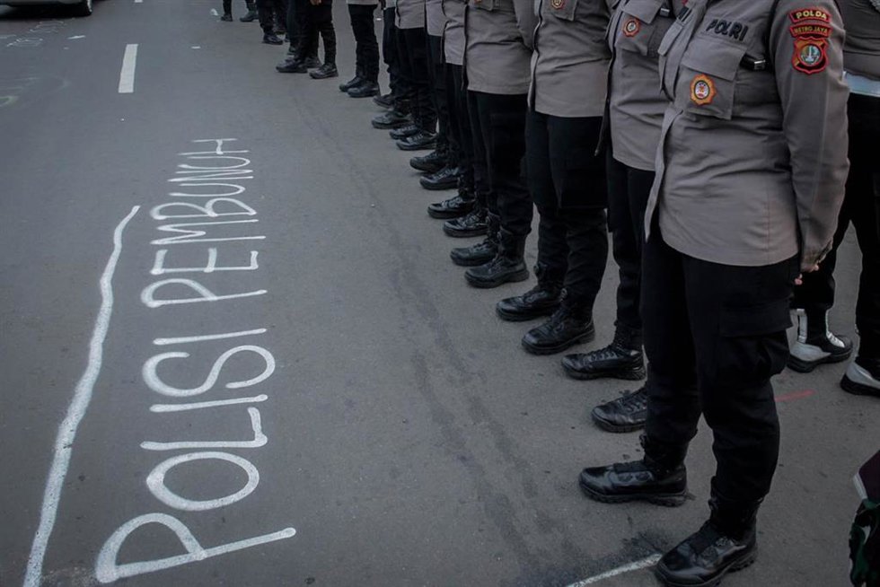 Agentes de la Policía en Indonesia frente a una pintada con la frase "Policía asesina"