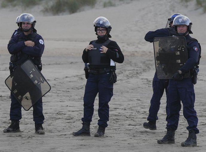 Archivo - Arquivo - 12 de agosto de 2025, Gravelines, França: Gravelines, França. Policiais com equipamento de choque observam migrantes enquanto tentam embarcar em um barco inflável na praia de Gravelines, antes de tentar atravessar o Canal da Mancha. O 