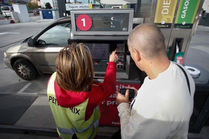 Archivo - Una trabajadora ayuda a un hombre a repostar combustible.