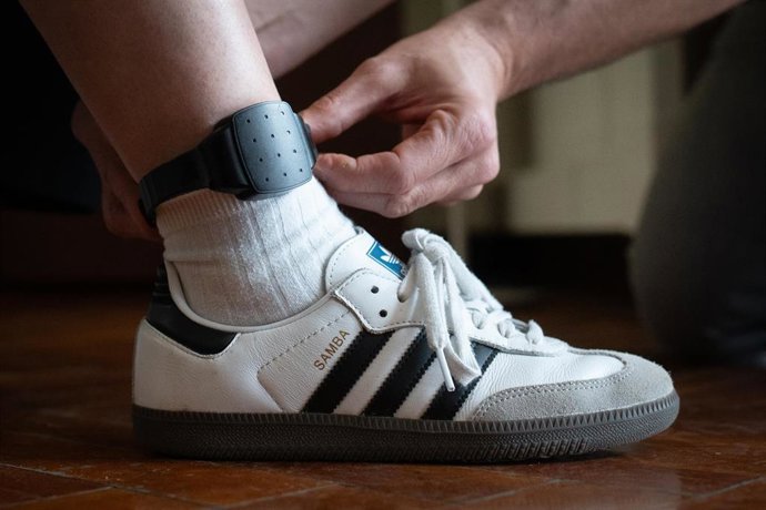 Archivo - Una persona le coloca a otra una pulsera electrónica de geolocalización telemática 