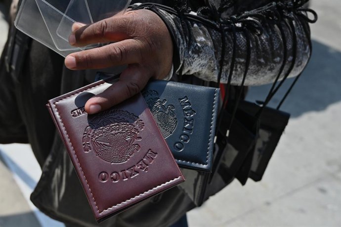 Archivo - 13 de agosto de 2025, Tijuana, Baja California, México: Um vendedor ambulante de capas de passaporte mostra uma capa de passaporte mexicano a trabalhadores mexicanos com vistos de trabalho que fazem fila perto do porto de entrada de San Ysidro, 
