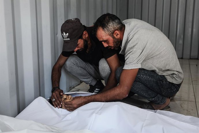 Palestinos no Hospital Al Auda, no campo de refugiados de Nuseirat, ao lado de um homem morto por ataques do exército israelense na Faixa de Gaza (arquivo).