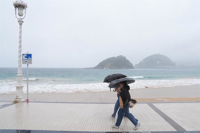 Archivo - Dos mujeres caminan con paraguas en la playa de Ondarreta