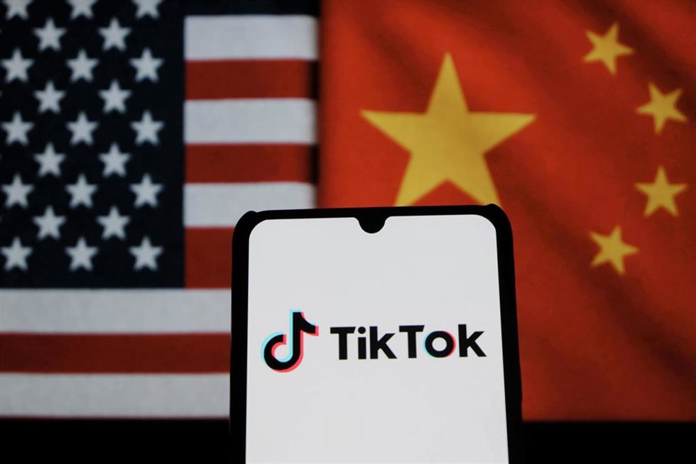 Logo de TikTok en un móvil con banderas estadounidenses y chinas de fondo.