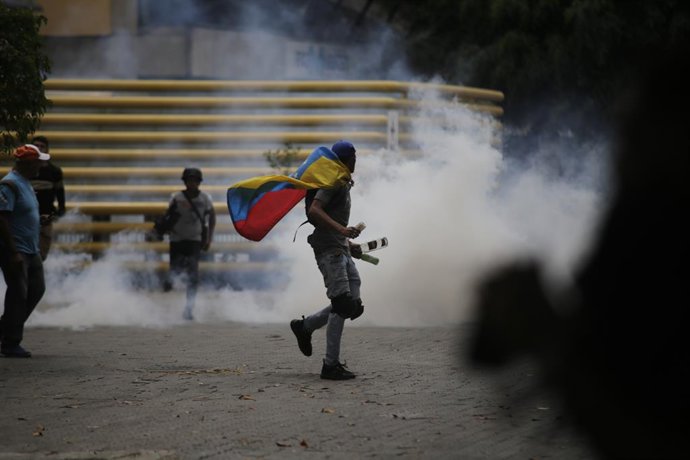 Archivo - 10 de março de 2020, Venezuela, Caracas: um manifestante enrolado em uma bandeira venezuelana corre durante um protesto contra o governo do presidente Maduro. Foto: Rafael Hernandez/dpa