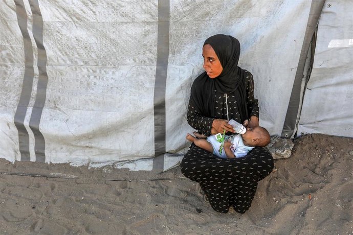 02 September 2025, Palestinian Territories, Khan Yunis: A woman feeds her kid next to a tent of displaced people after the displacement of Palestinians from Gaza City to the Mawasi area west of Khan Yunis in the southern Gaza Strip, following Israeli mili
