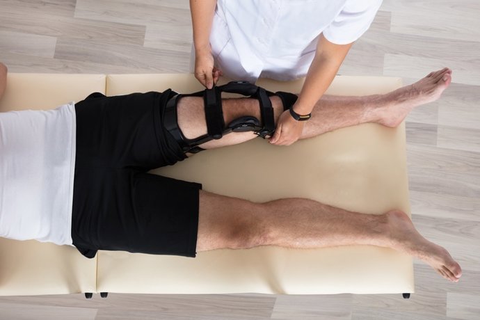 Archivo - Fisioterapeuta fixando joelheiras na perna de um homem