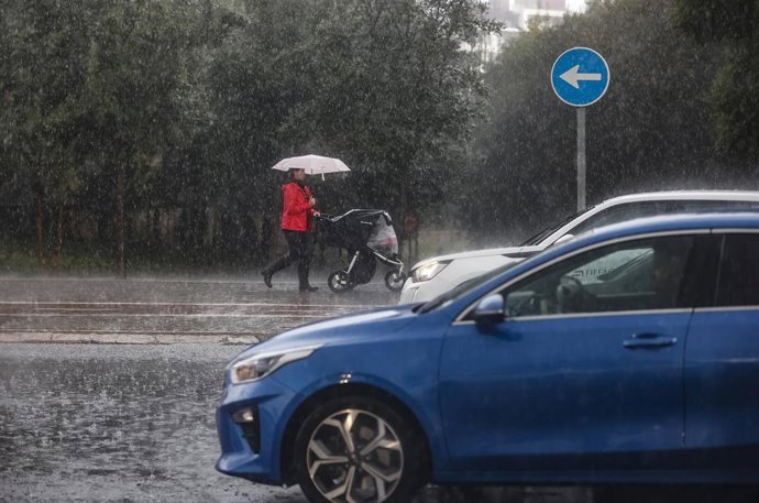 Archivo - Una mujer lleva un carrito de bebé mientras se protege de la lluvia en imagen de archivo