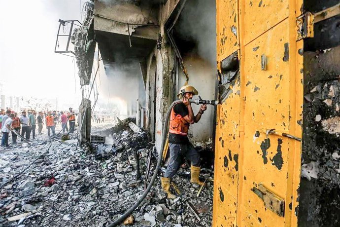 PALESTINA, GAZA Cidade de Gaza - 28 de setembro de 2025: Um bombeiro pulveriza água em um prédio danificado por um ataque aéreo israelense