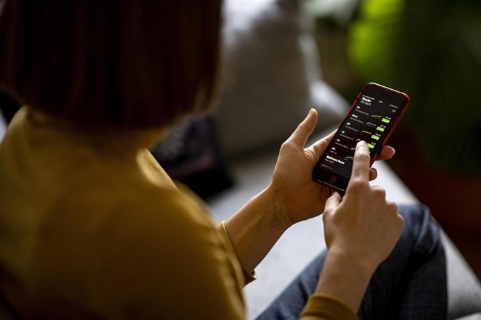 Archivo - FILED - 24 April 2021, Berlin: A young woman monitors share prices in an app on her smartphone.