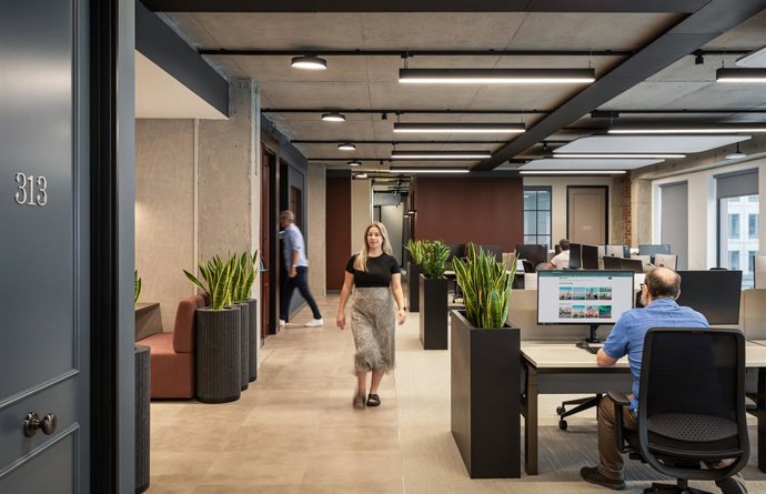 Co-workers sitting at a desk and walking within Tripadvisor's London office