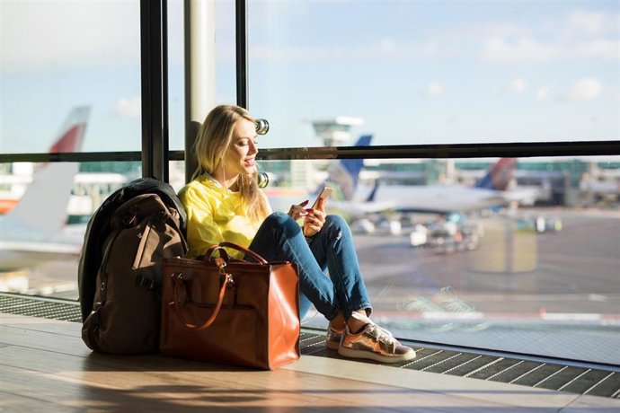 Archivo - Woman sitting in airport and waiting for her flight, woman using phone in airport departure area
