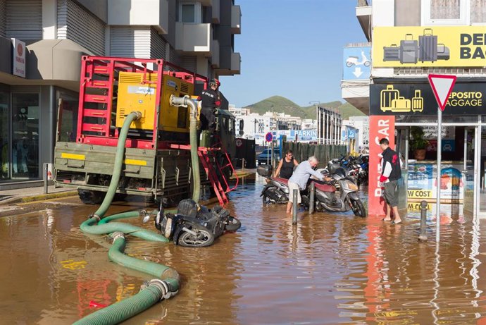 Varias personas y la UME apartan motos de una calle anegada de agua tras las lluvias
