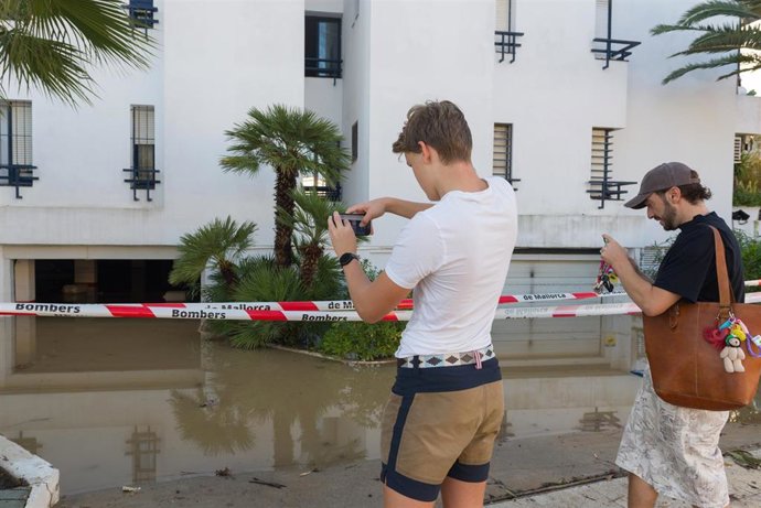 Dos hombre fotografían una calle anegada de agua tras las lluvias en Ibiza.