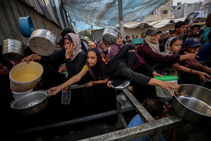 4 de outubro de 2025, Nuseirat, Nuseirat, Território Palestino: Palestinos, incluindo crianças, que estão lutando para ter acesso a alimentos devido aos contínuos ataques israelenses, recebem refeições quentes distribuídas pela organização de caridade no 