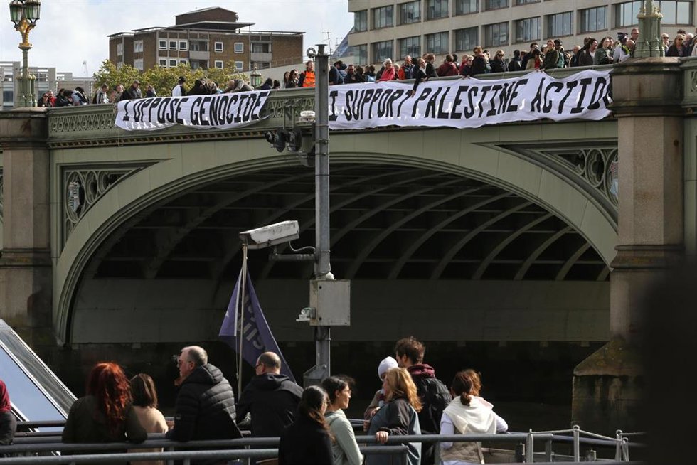Un grupo de activistas sostiene dos pancartas en el lateral del puente de Westminster con el lema "Me opongo al Genocidio y Apoyo la Acción Palestina" durante un acto de protesta, rodeados de policías, en Londres, Reino Unido