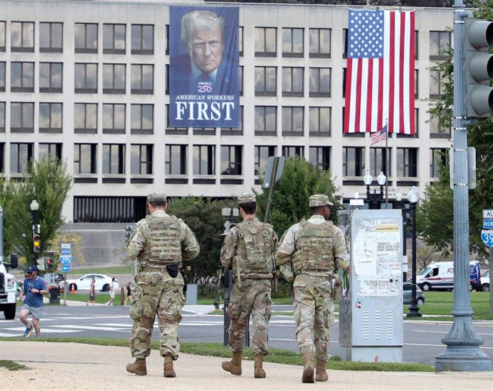Archivo - Miembros de la Guardia Nacional patrullan a lo largo del National Mall cerca del Capitolio de Estados Unidos, bajo una pancarta propagandística del presidente del país, Estados Unidos