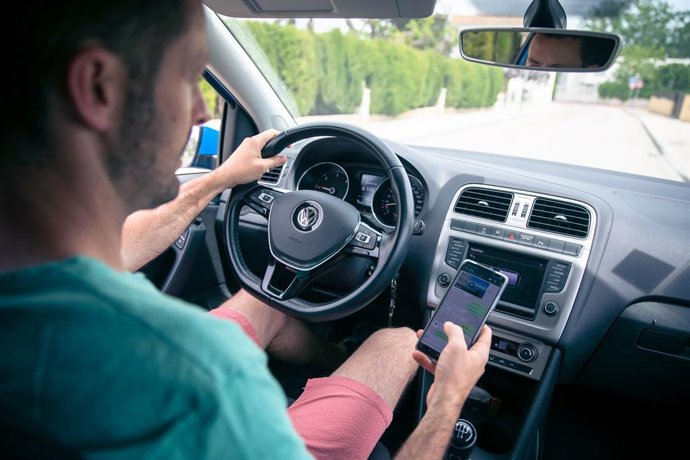 Un home mirant el mòbil i conduint