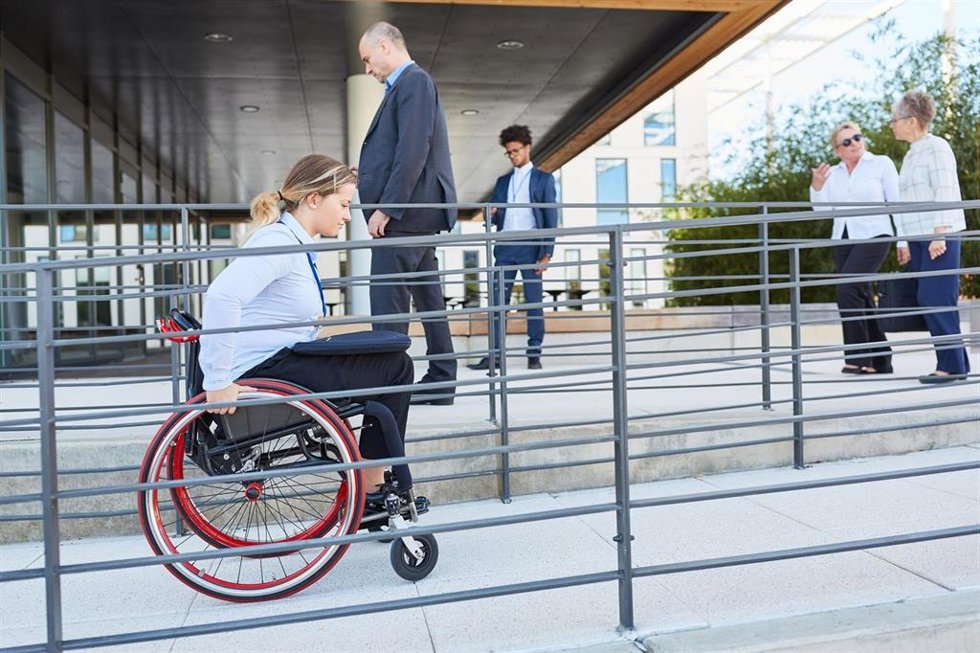 Archivo - Una mujer avanza en silla de ruedas por una rampa adaptada en un edificio público.