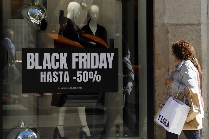 Archivo - Dos personas observan el cartel de una tienda con descuentos por el Black Friday.