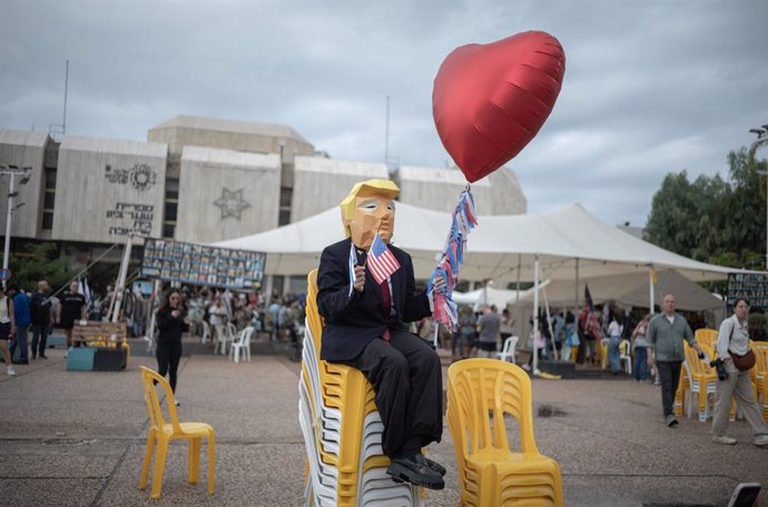 09 October 2025, Israel, Tel Aviv: A person wears a mask that resembles US President Trump and holds the US flag and a heart shaped balloon as people gather at hostage square in Tel Aviv to celebrate the ceasefire deal. After 2 years of war, Israel and Ha