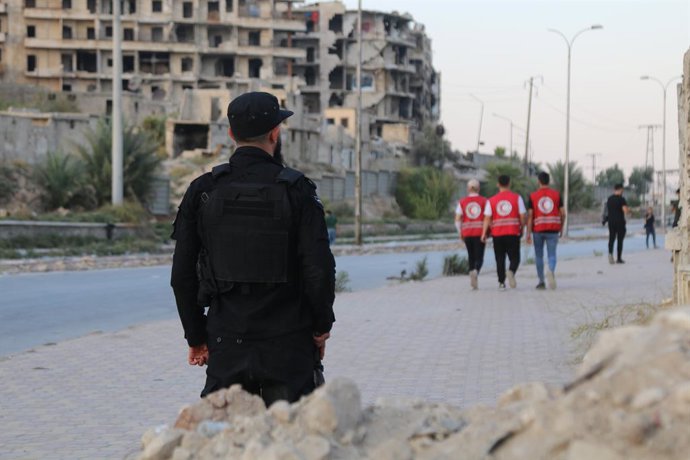 DAMASCUS, 7 de outubro de 2025 -- Um membro do Comando de Segurança Interna fica perto de prédios danificados nos bairros Sheikh Maqsoud enquanto voluntários do Crescente Vermelho Árabe Sírio passam em Aleppo, Síria, em 7 de outubro de 2025. O chefe da au