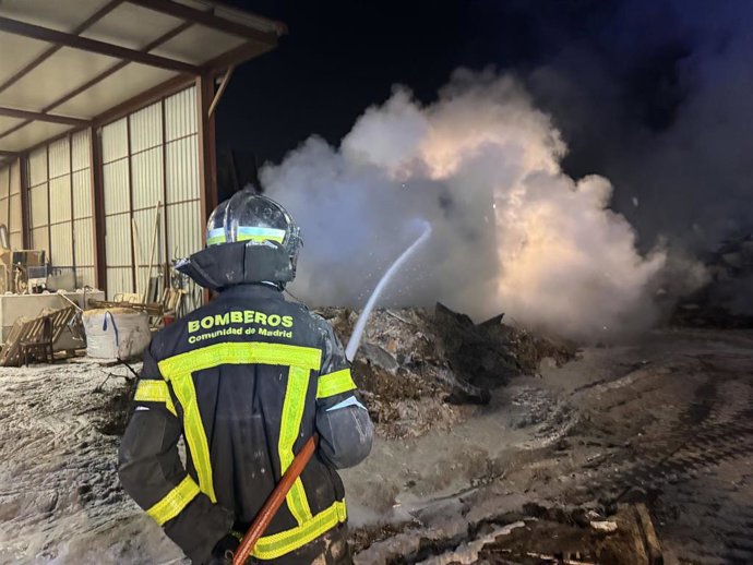 Un bombero de la Comunidad de Madrid trata de extinguir un incendio en una parcela de reciclaje de madera en San Fernando de Henares