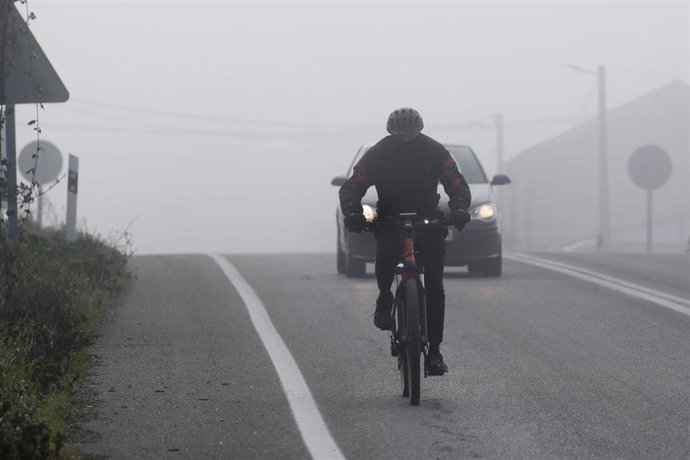 Archivo - Un ciclista y un coche en una carretera con niebla.