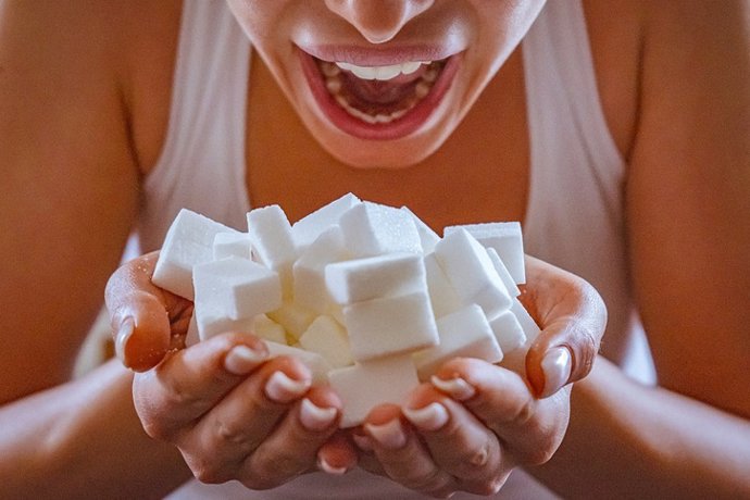 Archivo - Close-up of woman holding a hands full of sugar cubes in front of her open mouth