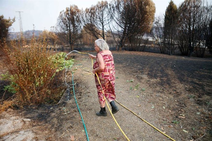 Archivo - Una mujer refresca el terreno para que no se reproduzca el fuego, como foto de recurso.