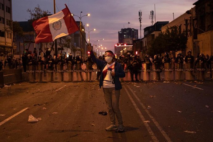 Archivo - Una manifestante porta un bandera en las calles de Lima ante un pelotón de la Policía