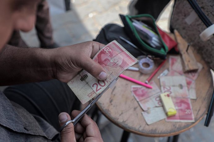 Archivo - KHAN YOUNIS, Oct. 1, 2024  -- A Palestinian man repairs worn-out bills in the southern Gaza Strip city of Khan Younis, on Sept. 30, 2024. TO GO WITH "Feature: Lack of cash, banking services double suffering for Gazans"