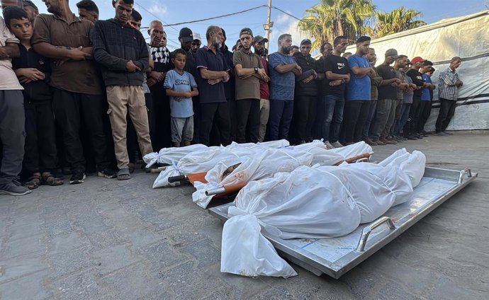 Un grupo de personas contemplan los cuerpos de otros gazatíes fallecidos en un ataque israelí, frente el hospital Shuhada al Aqsa de Deir al Balá, en el centro de la Franja de Gaza