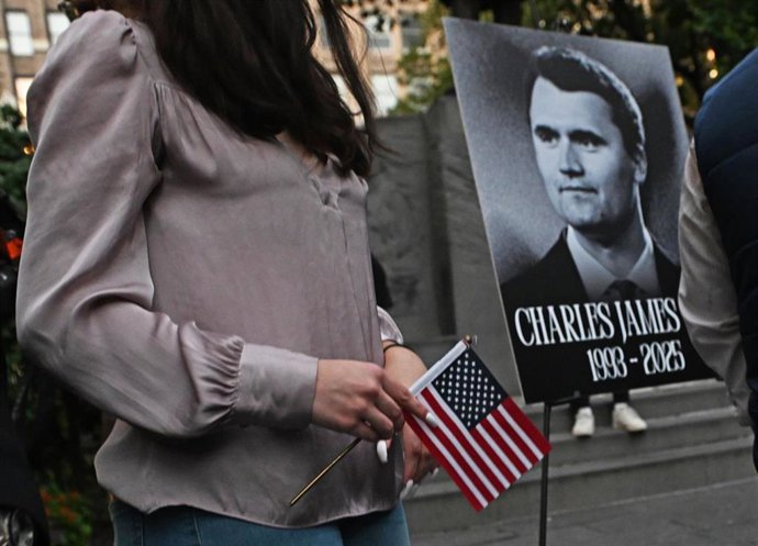 Archivo - 12 September 2025, US, New York: A woman holds a US flag next to a photo of Charlie Kirk, the US conservative activist and co-founder of Turning Point USA, who was shot dead at an event at Utah Valley University