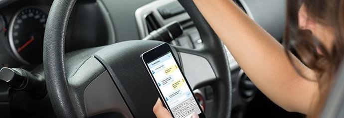 Archivo - Una conductora usa un teléfono móvil mientras conduce su vehículo.