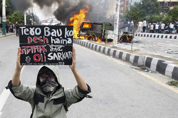 Archivo - Arquivo - 8 de setembro de 2025, Katmandu, Nepal: Um jovem manifestante da Geração Z segura um cartaz em frente a um veículo incendiado em Katmandu, Nepal, na segunda-feira, 8 de setembro de 2025. Os manifestantes se reuniram contra a corrupção 