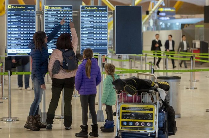 Archivo - Varias personas observan las salidas de los vuelos en un aeropuerto.