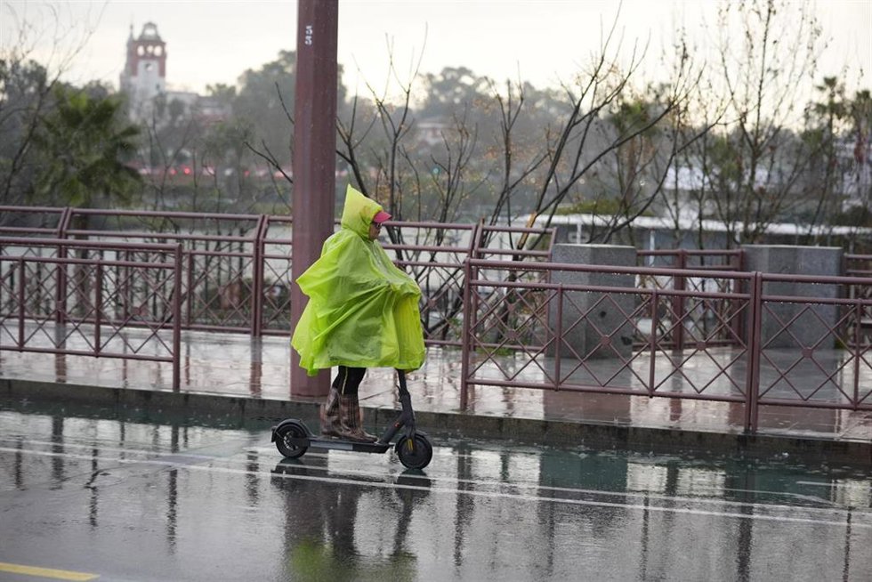 Archivo - Una persona se protege de la lluvia con un impermeable en Sevilla. Imagen de archivo.