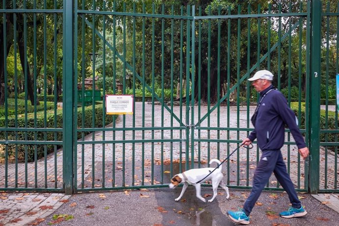 Un hombre pasea a su perro junto a uno de los parques de la ciudad, cerrado por los avisos de fuertes lluvias y vientos.